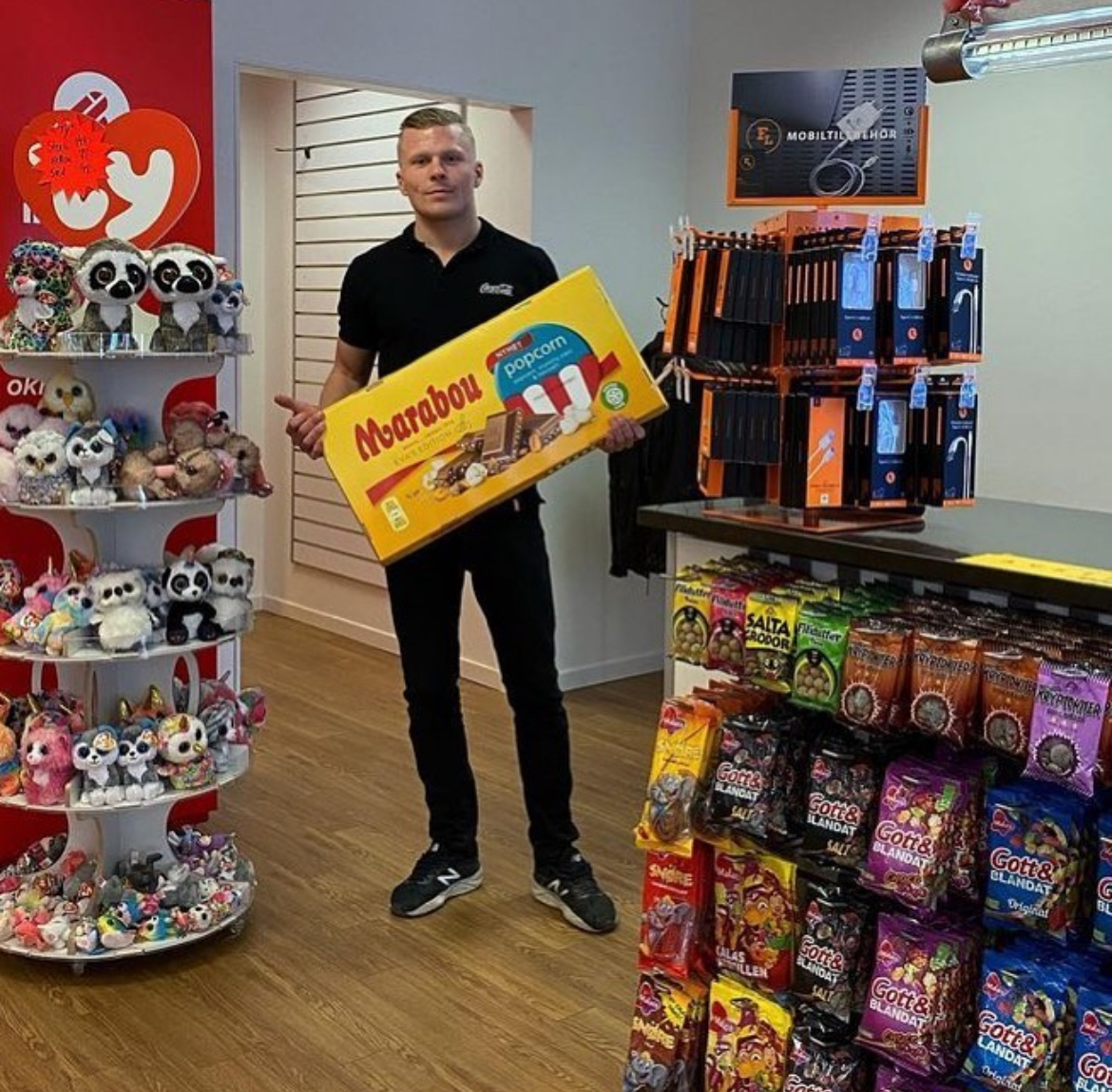 Medarbetare i butiken håller upp en stor chokladask framför gosedjur och godishyllor